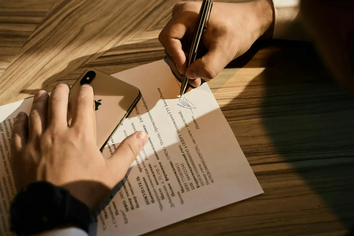 Persona firmando una carta sobre una mesa de madera