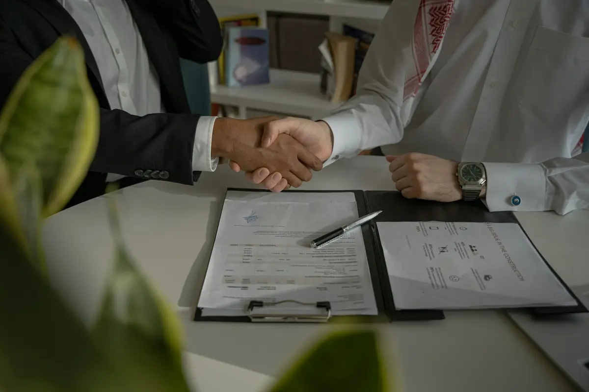 Dos profesionales se dan la mano sobre una mesa con contratos y documentación laboral
